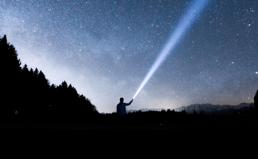 Person silhouette shining flashlight over nighttime starry sky