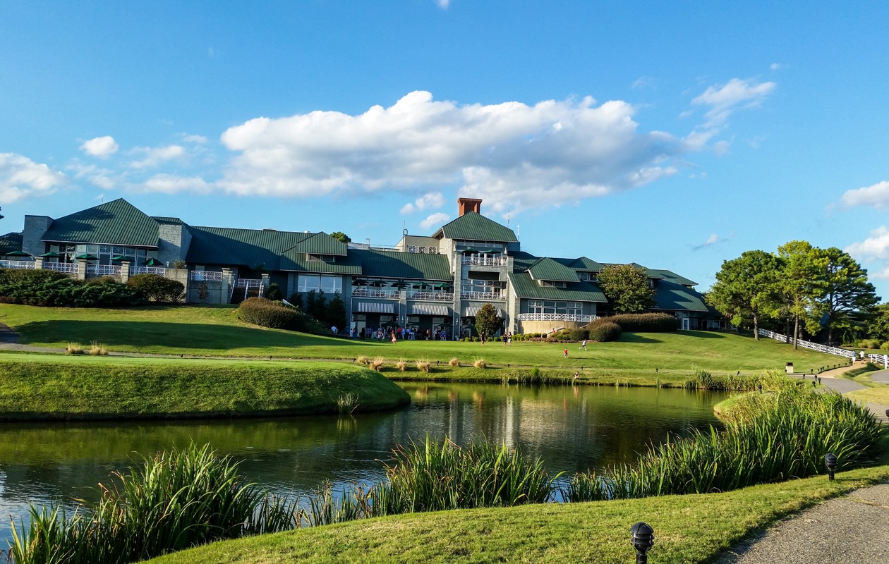 Landscape orientation photo of Kingsmill Resort grounds and building in summer. The resort sits in the background with a pond and lush green grass in the foreground.