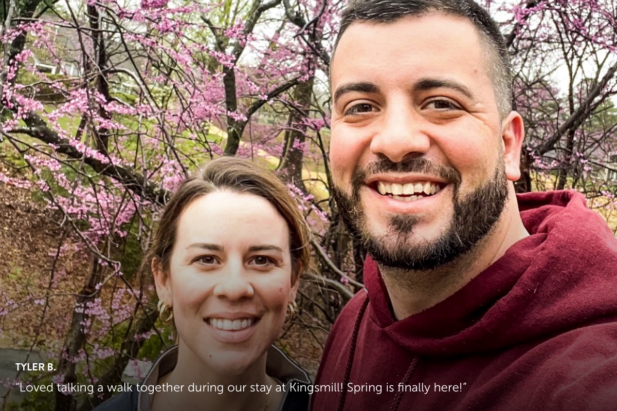 Photo submission from Tyler B., showing a man and woman smiling outside in front of springtime cherry blossoms.